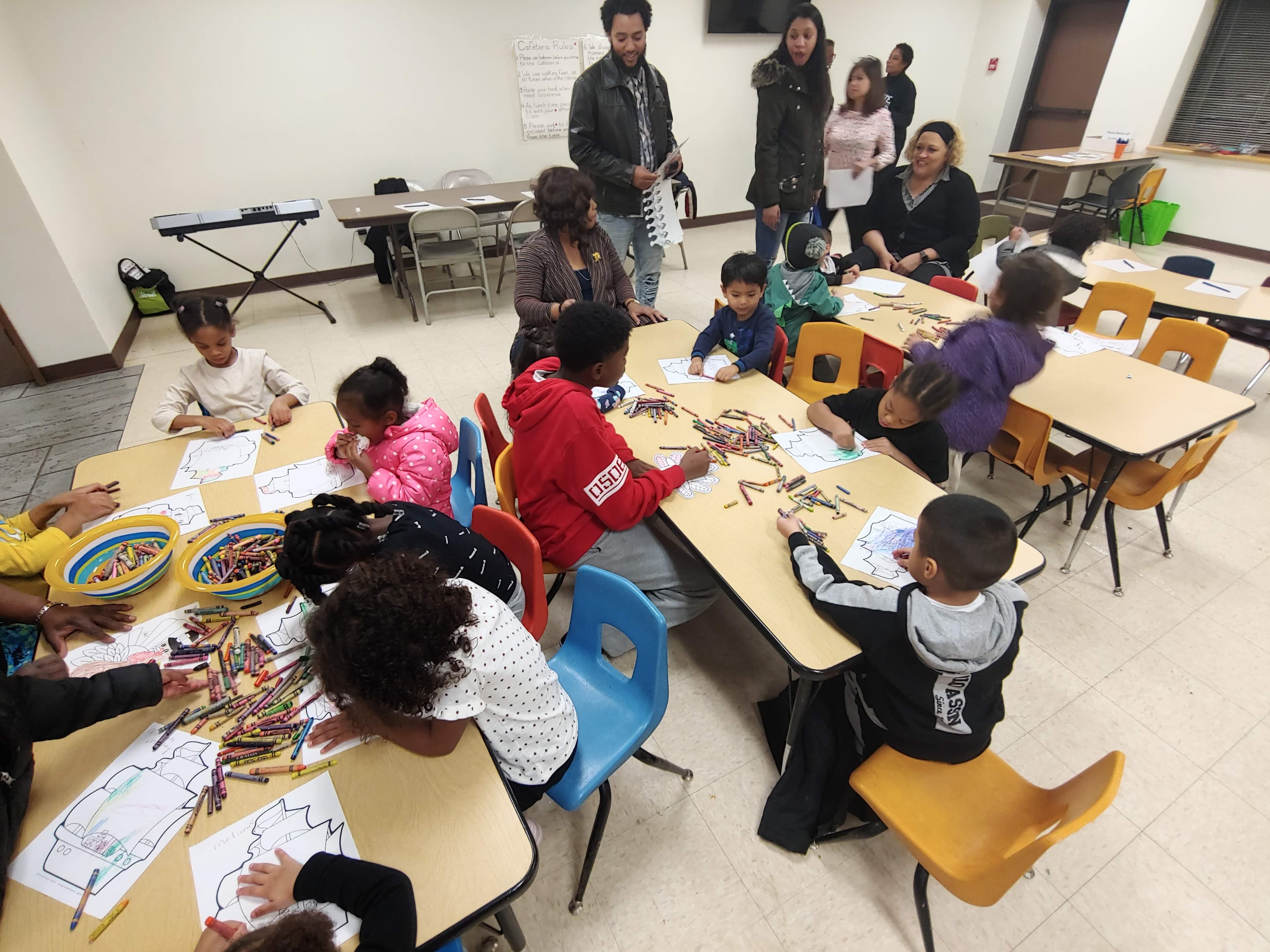 Children color at cafeteria tables covered in crayons while parents and staff look on during a family night.